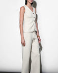 Woman wearing a white sleeveless top and wide-leg pants against a plain background