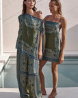 Two women wearing matching green and blue patterned dresses by a pool.