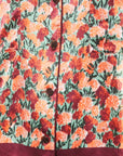 Close-up of a floral-patterned garment, likely a jacket or coat, featuring orange, red, and yellow flowers with green leaves on a light background, with dark buttons and a dark burgundy border at the bottom.