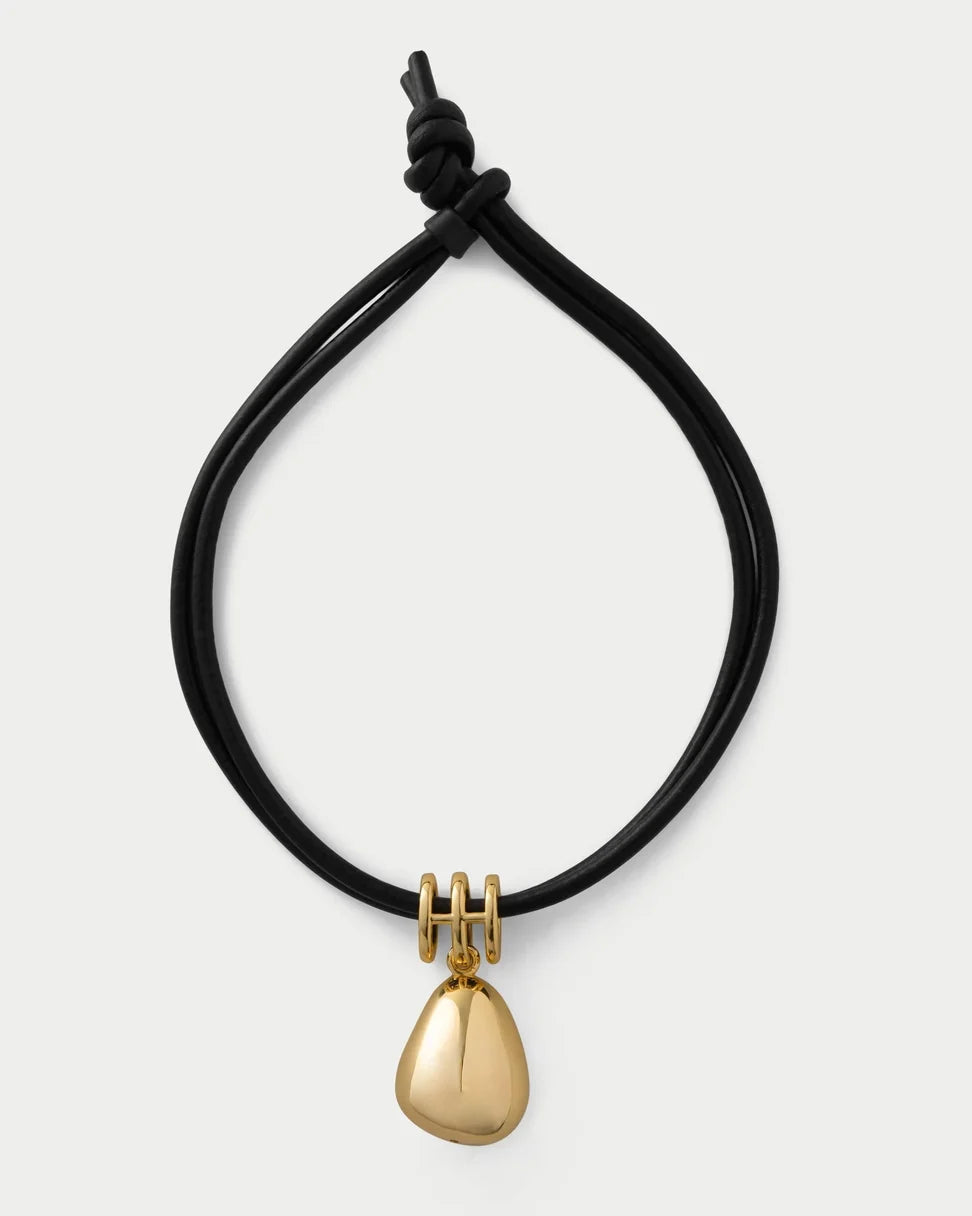 A black adjustable cord bracelet with a polished gold teardrop pendant and gold ring details, shown on a light gray background.