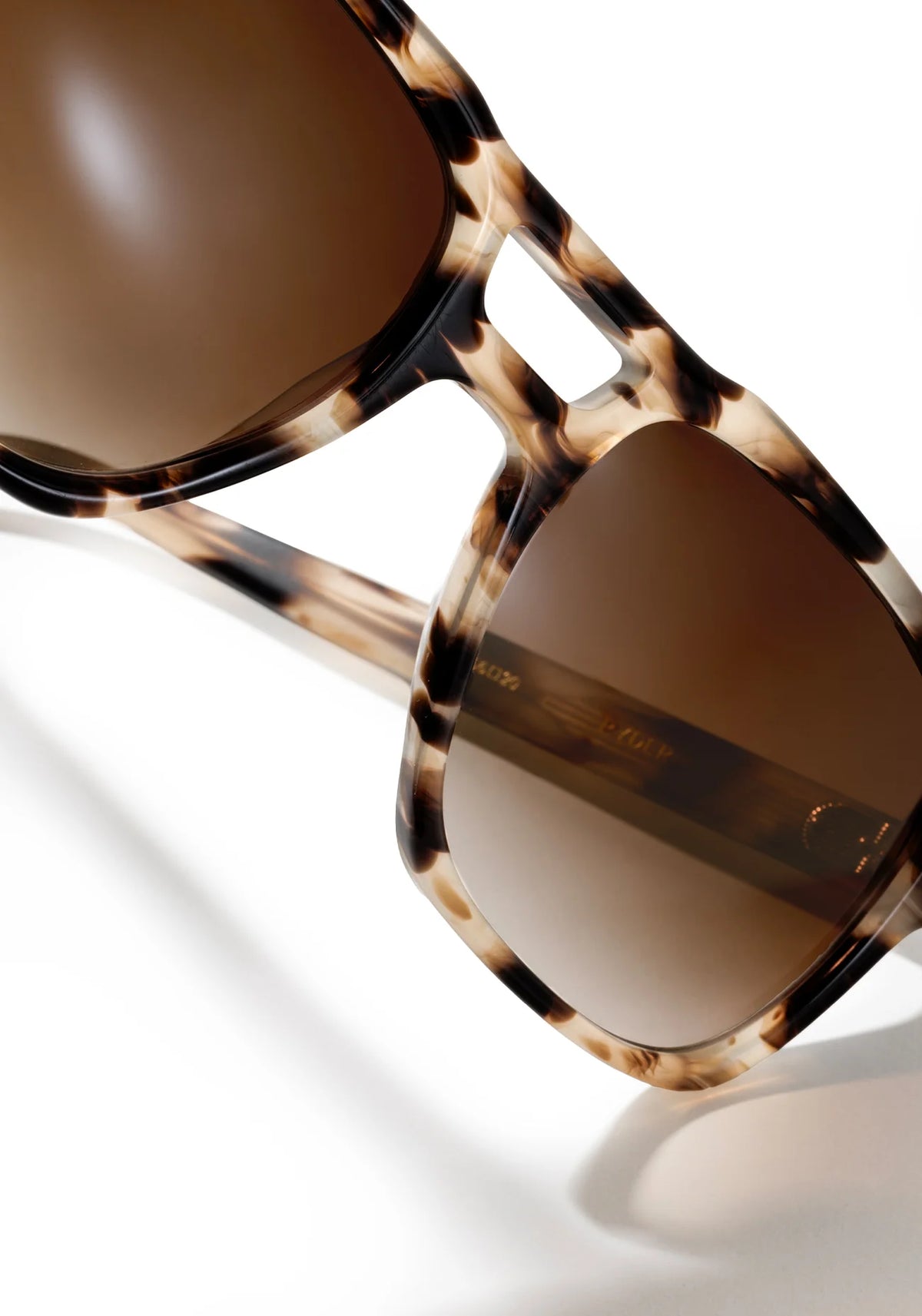 Close-up of tortoiseshell sunglasses with brown tinted lenses on a clean white background.