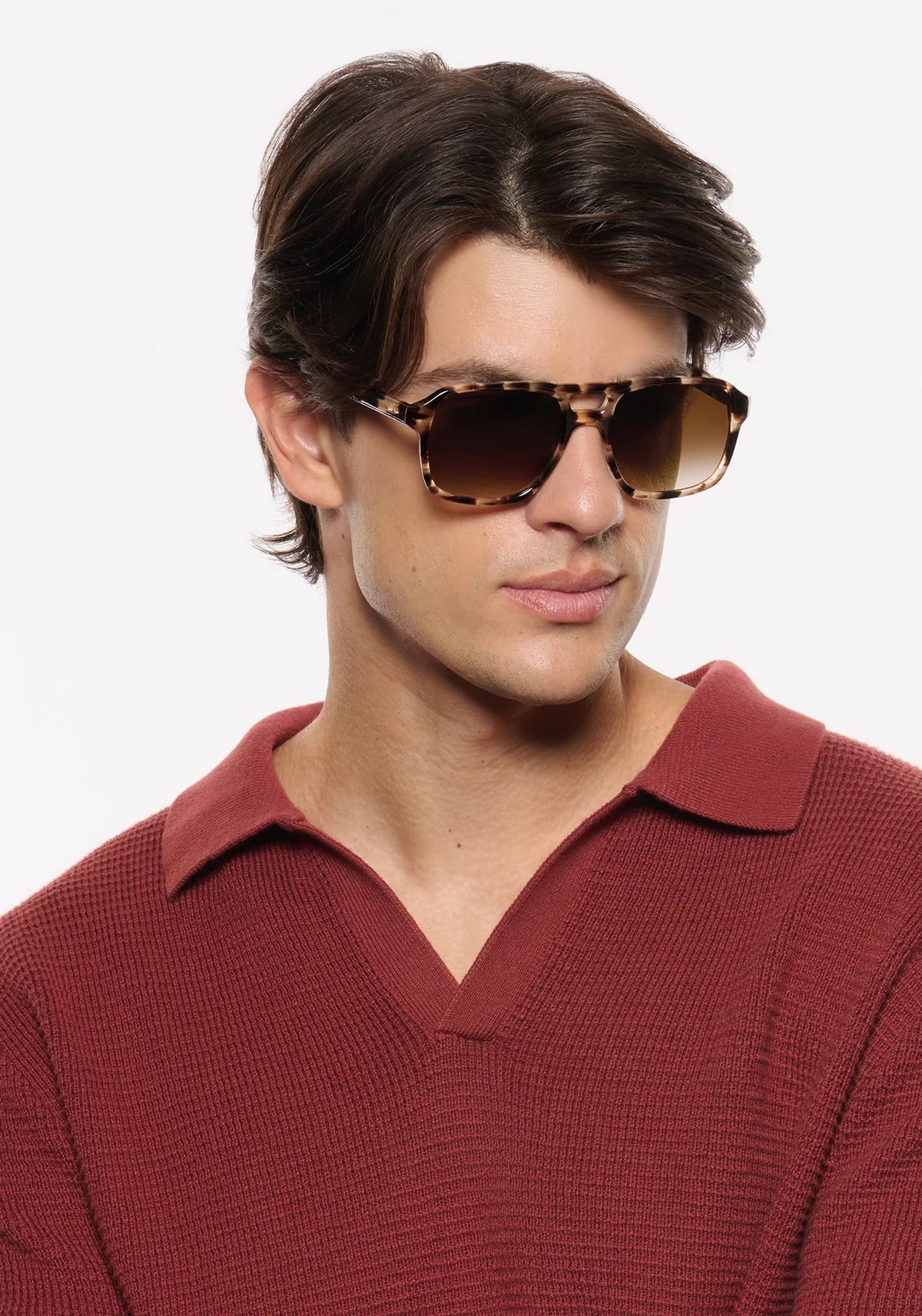 A man wearing tortoiseshell aviator-style sunglasses with brown lenses and a textured burgundy knit polo shirt, photographed against a clean white background.