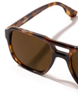 Close-up of a pair of sunglasses with a tortoiseshell acetate frame and dark brown lenses, showing the brand name Krewe on the inner temple arm, set against a clean white background.
