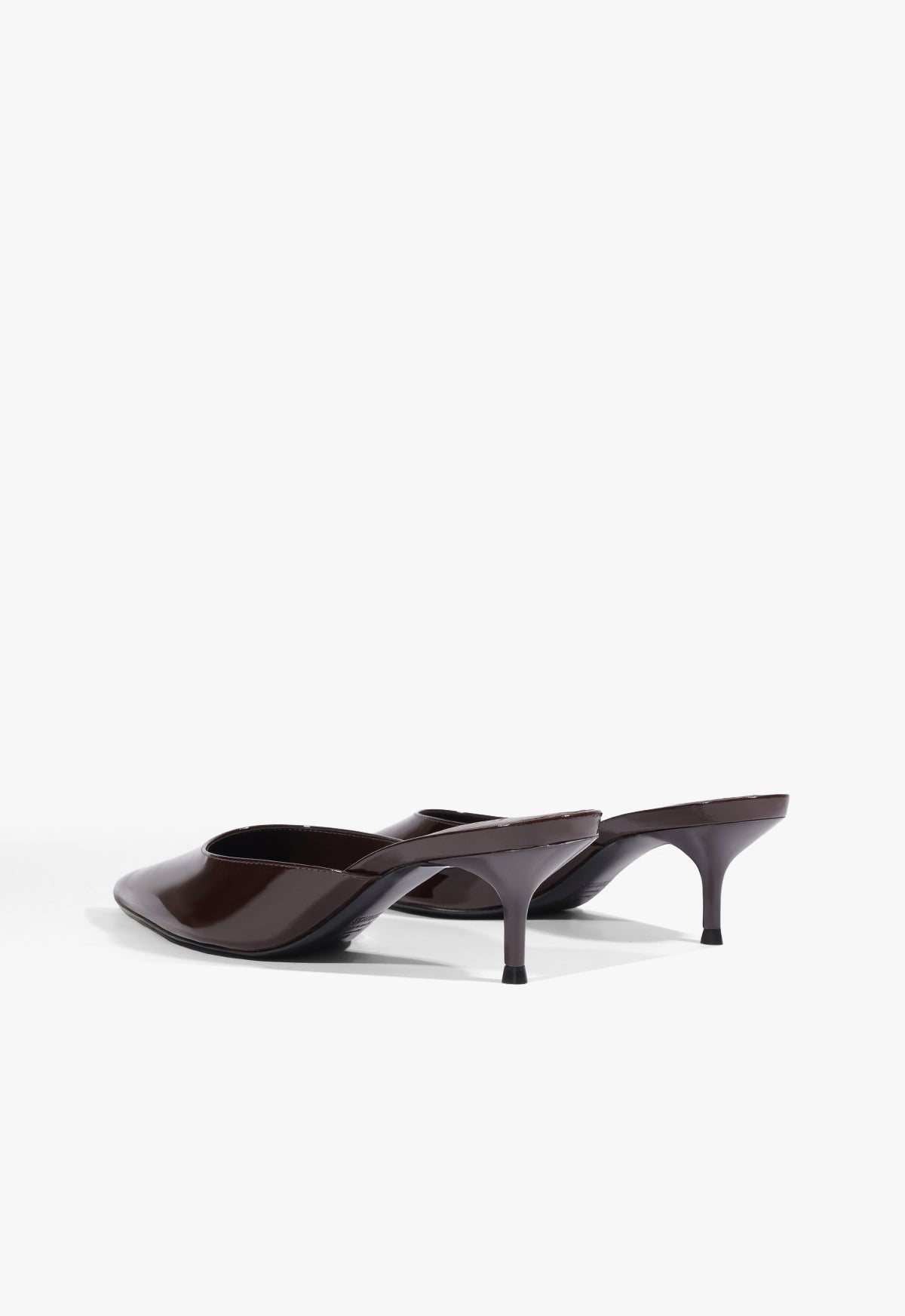 A pair of dark brown patent leather mule heels with kitten heels, shown from a side profile view on a light gray studio background.