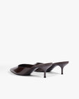 A pair of dark brown patent leather mule heels with kitten heels, shown from a side profile view on a light gray studio background.