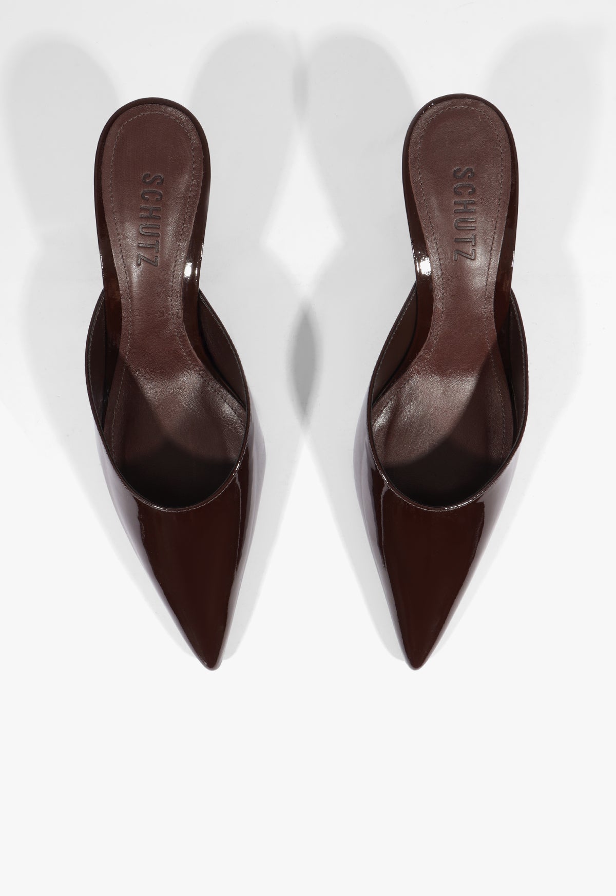 A pair of dark brown pointed-toe mule heels with a glossy finish, shown from a top-down perspective on a light gray background.
