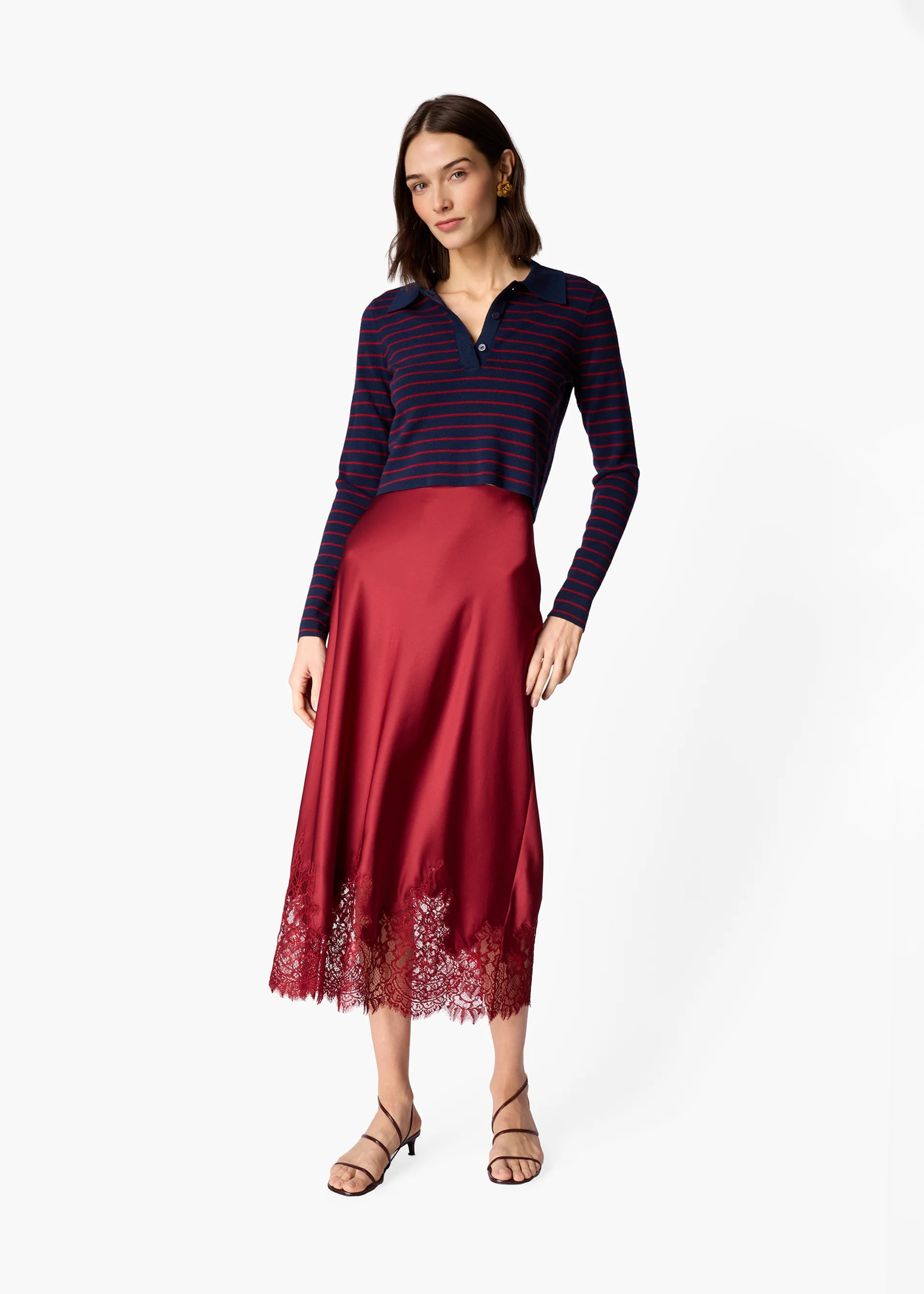 A woman modeling a long-sleeve knit top with navy and red horizontal stripes paired with a red satin midi skirt featuring a lace hem, against a plain light gray background.