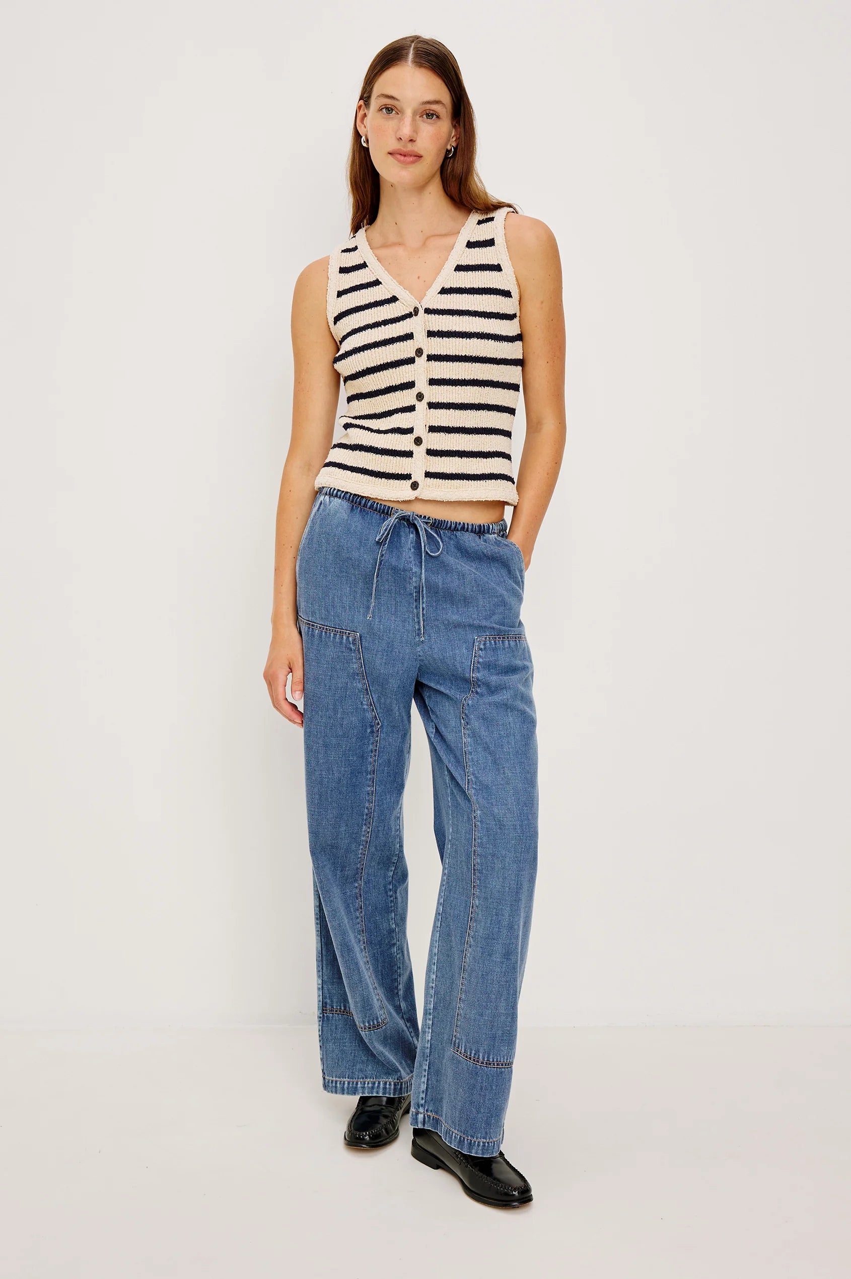 Woman wearing a striped sleeveless top and blue jeans on a white background