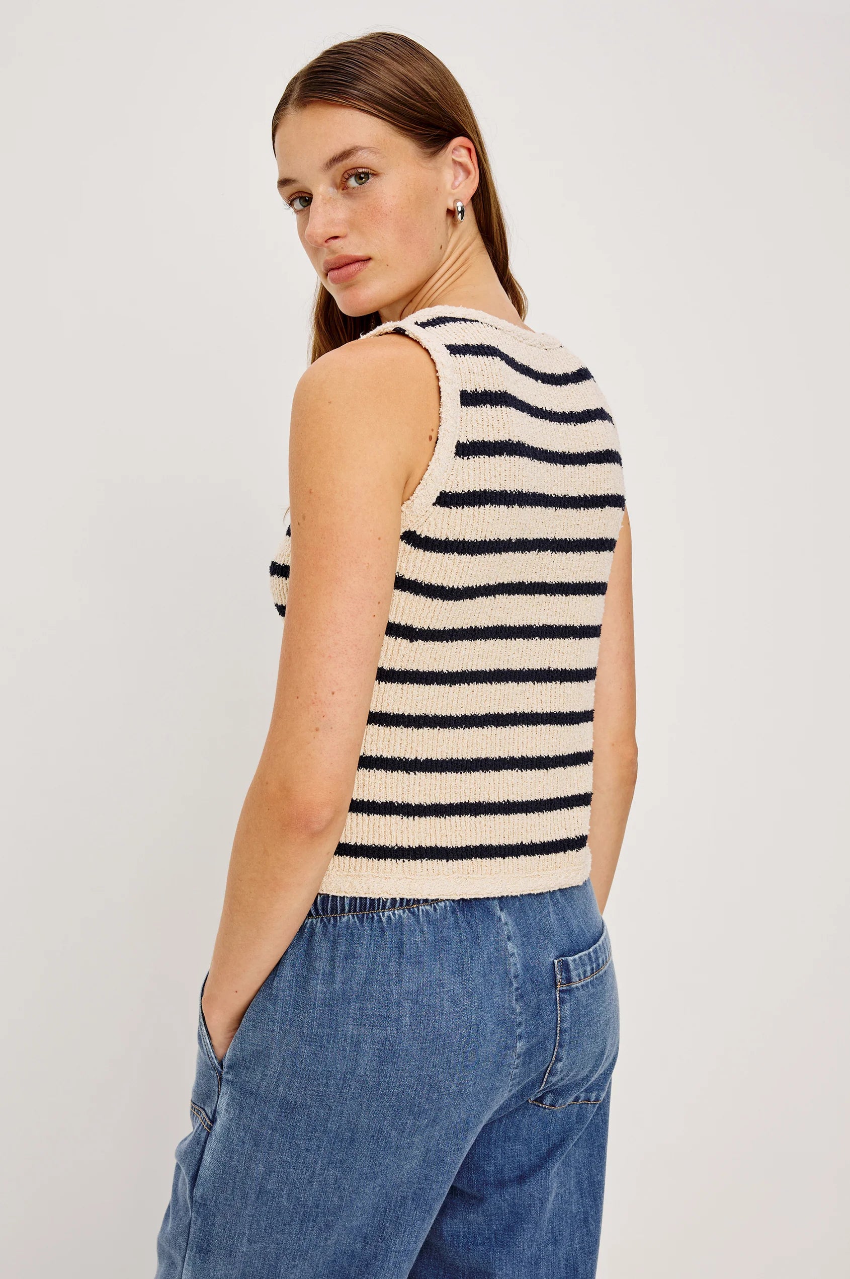 Woman wearing a black and white striped sleeveless top with blue jeans on a plain background