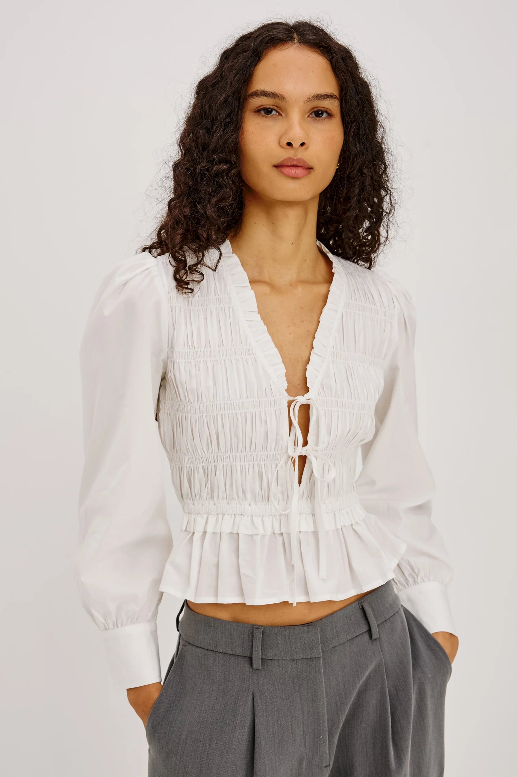 Woman wearing a white blouse with a deep neckline and gray pants on a light gray background