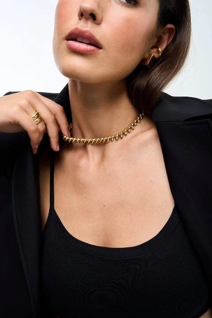 Woman wearing a gold necklace and ring against a neutral background
