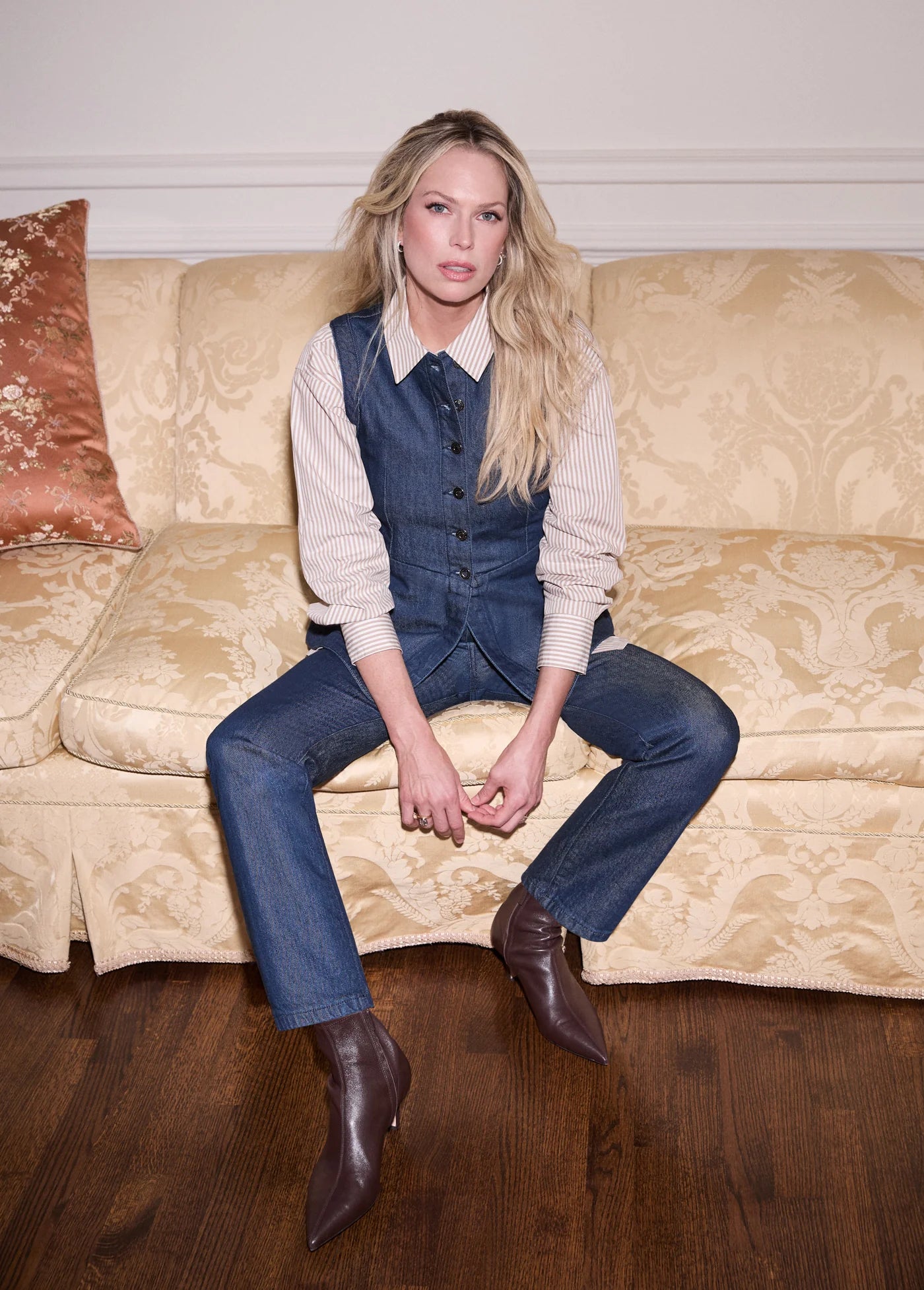 Woman sitting on a beige couch wearing a denim outfit.
