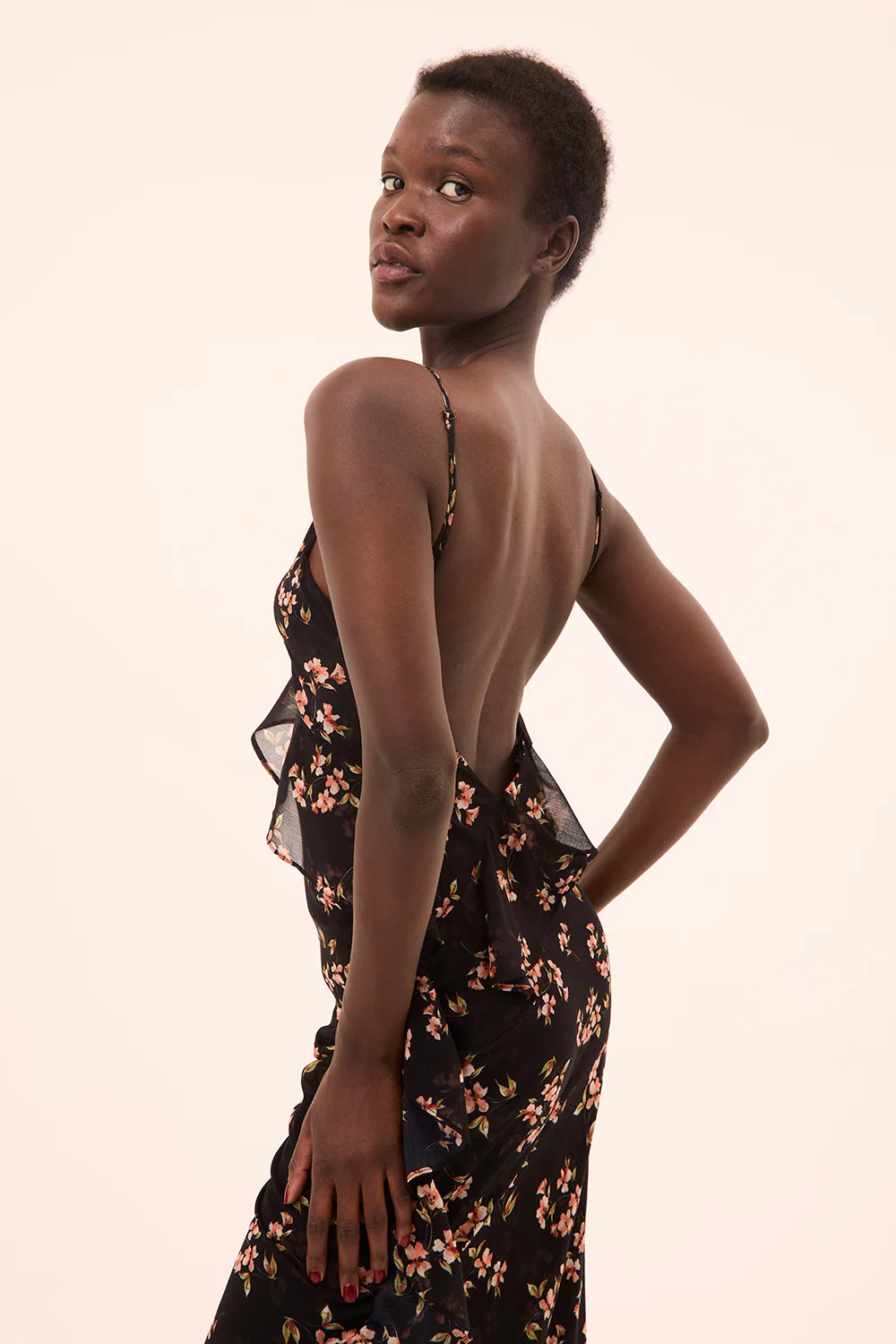 Woman wearing a floral dress with a plain background, side view
