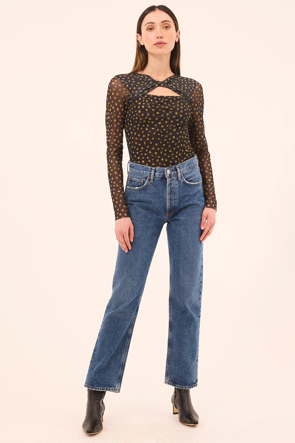 Woman wearing a black polka dot long-sleeve top and blue jeans on a beige background