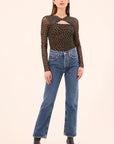 Woman wearing a black polka dot long-sleeve top and blue jeans on a beige background