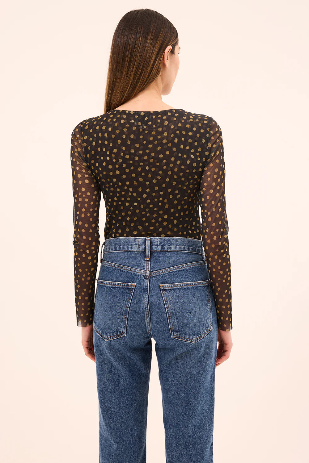 Person wearing a polka dot long-sleeve top and blue jeans on a beige background