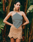 Woman wearing a striped halter top and beige crochet skirt in a tropical setting