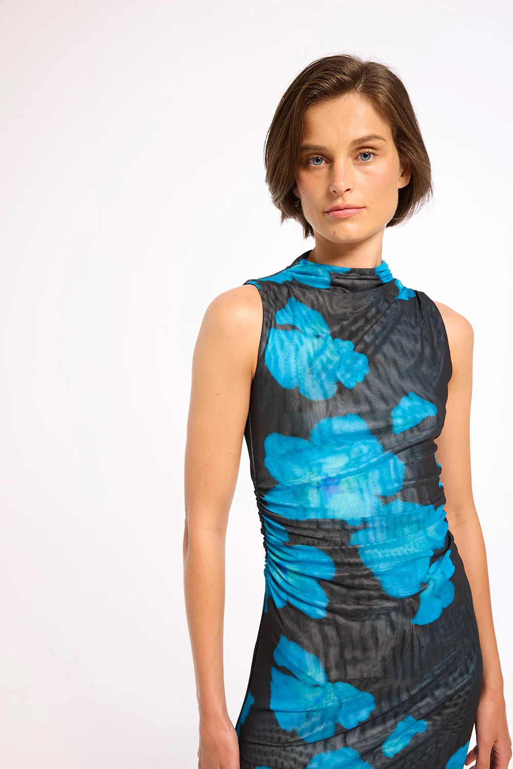 A woman modeling a sleeveless mock-neck dress with a high-contrast blue and black abstract floral pattern, photographed against a clean white studio background.