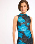 A woman modeling a sleeveless mock-neck dress with a high-contrast blue and black abstract floral pattern, photographed against a clean white studio background.