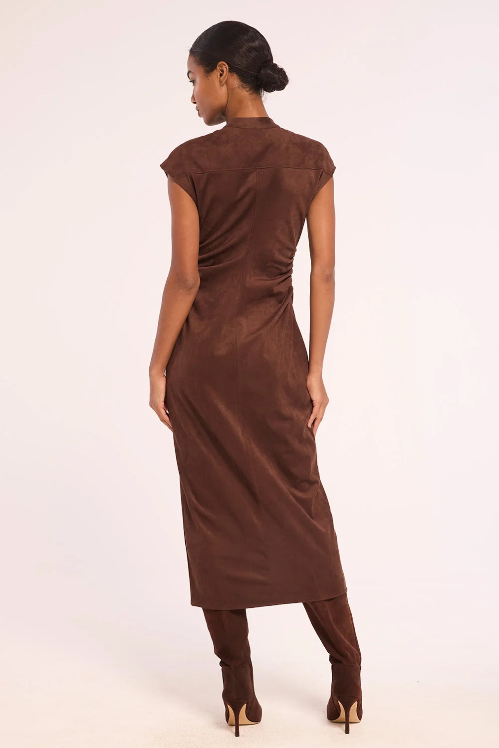 A woman shown from the back wearing a brown sleeveless midi dress with gathered side details, paired with matching brown boots, against a plain light background.