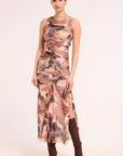 A woman modeling a sleeveless ruched midi set with an abstract floral print in shades of brown, beige, and pink, paired with brown boots, against a plain light background.