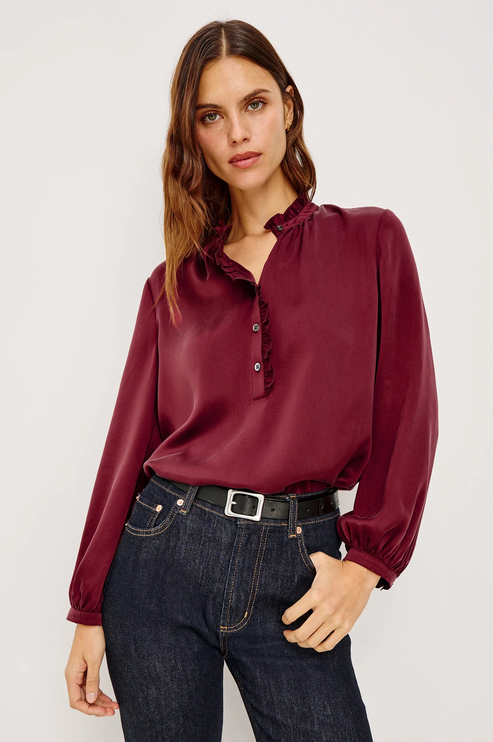 Woman wearing a burgundy blouse and dark jeans against a white background