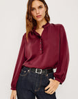 Woman wearing a burgundy blouse and dark jeans against a white background