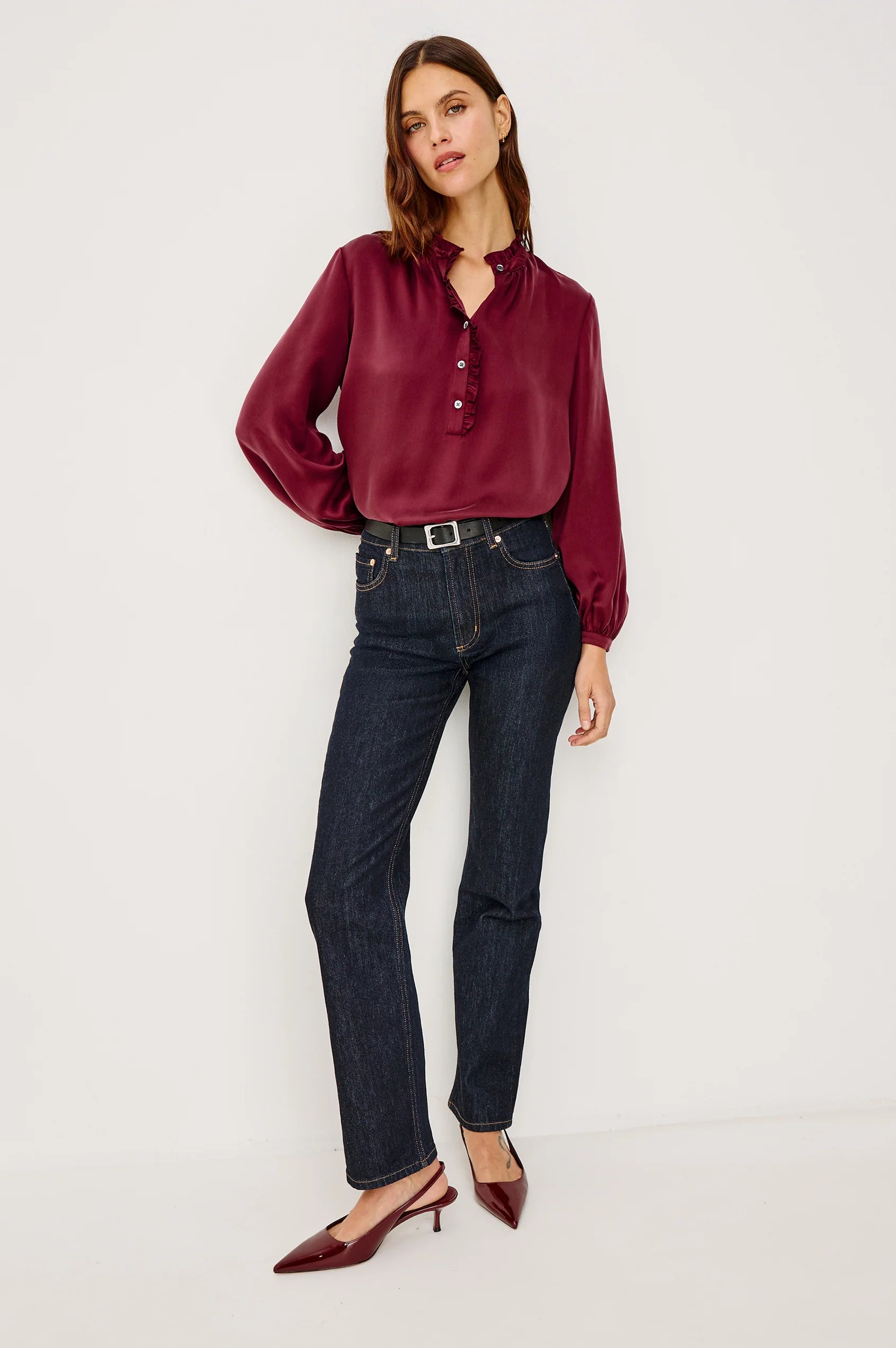 Woman wearing a burgundy blouse and dark jeans on a white background