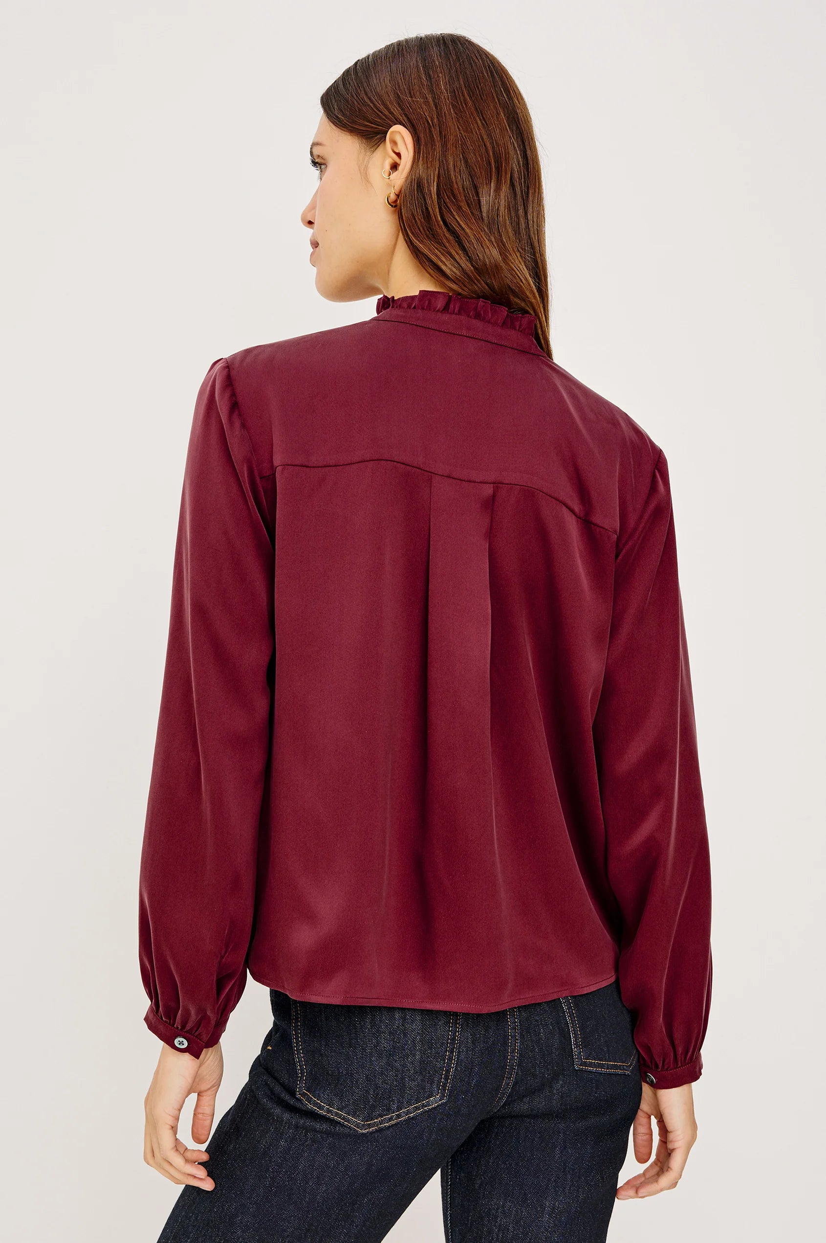 Person wearing a burgundy blouse and dark jeans on a white background
