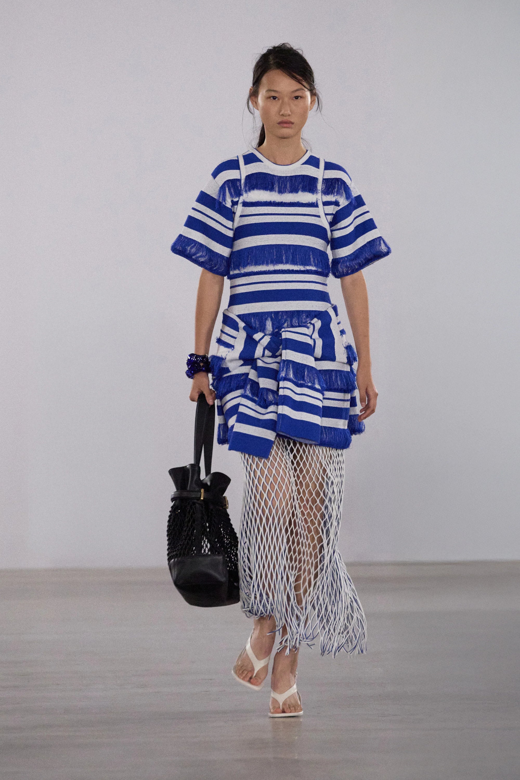 Model wearing a blue and white striped dress with a black handbag on a plain background