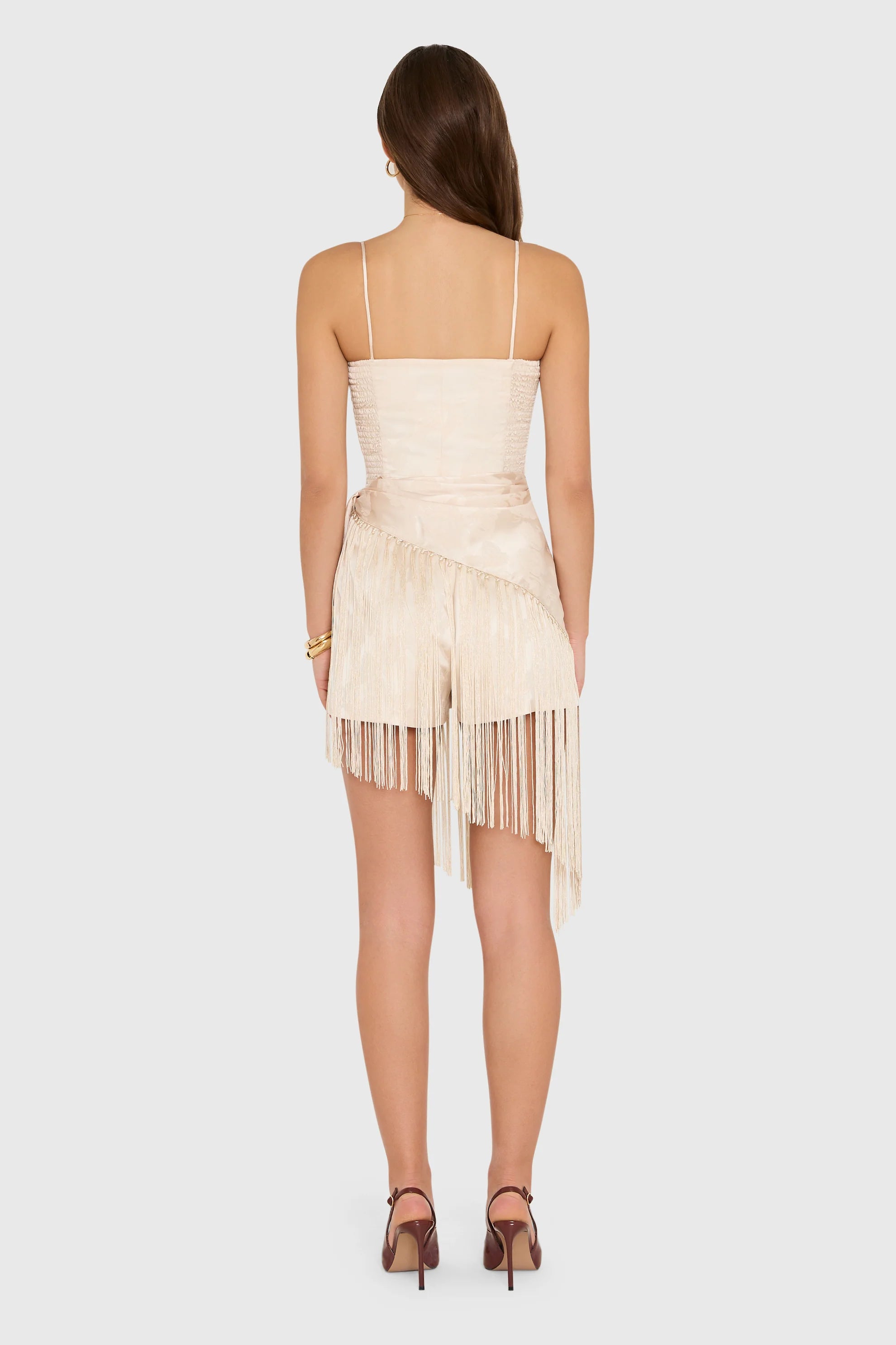 model wearing a cream colored romper with fringe scarf detail, back view
