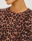 Close-up of a person wearing a fuzzy knit top with a leopard print pattern in brown and black on a dusty pink background.