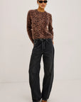 Person wearing a leopard print sweater and black jeans on a white background