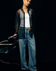 Woman wearing Sofiya Sheer Top, white top, and blue jeans against a black background