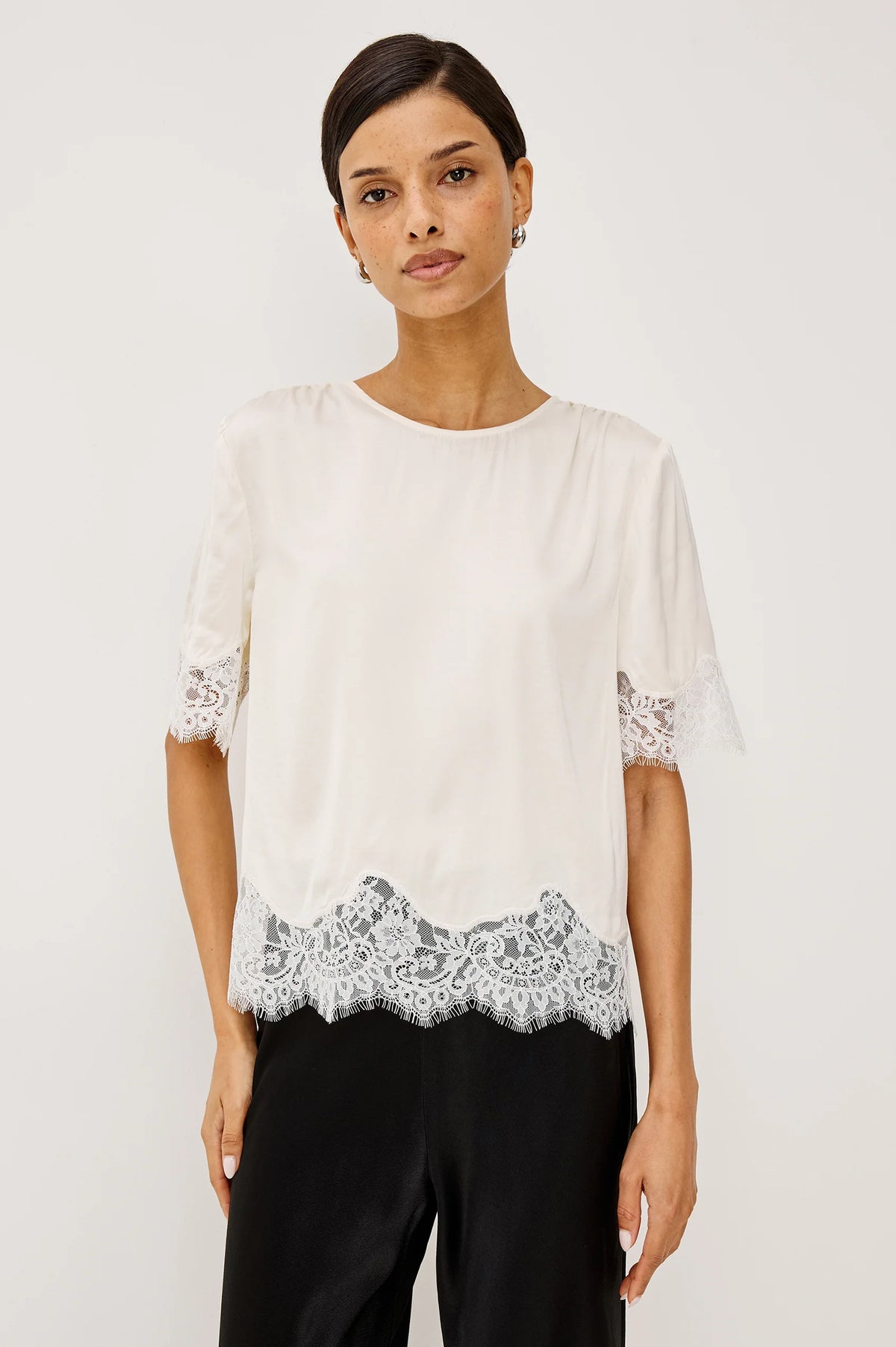 Woman wearing a white blouse with lace details on a plain background