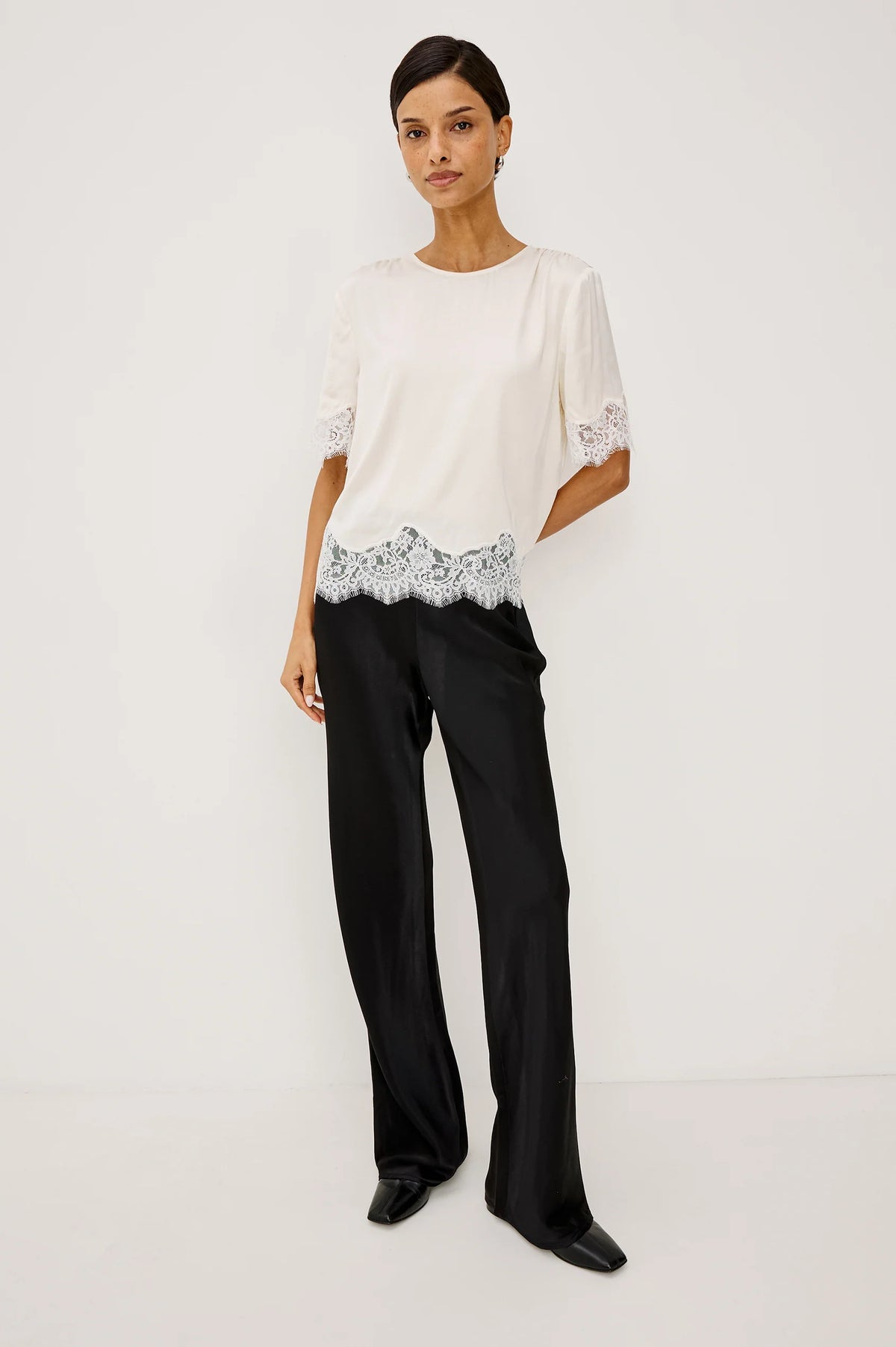 Woman wearing a white blouse with lace details and black pants on a light gray background