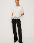 Woman wearing a white blouse with lace details and black pants on a light gray background