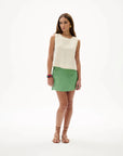 Woman wearing a white sleeveless top and green skirt on a white background