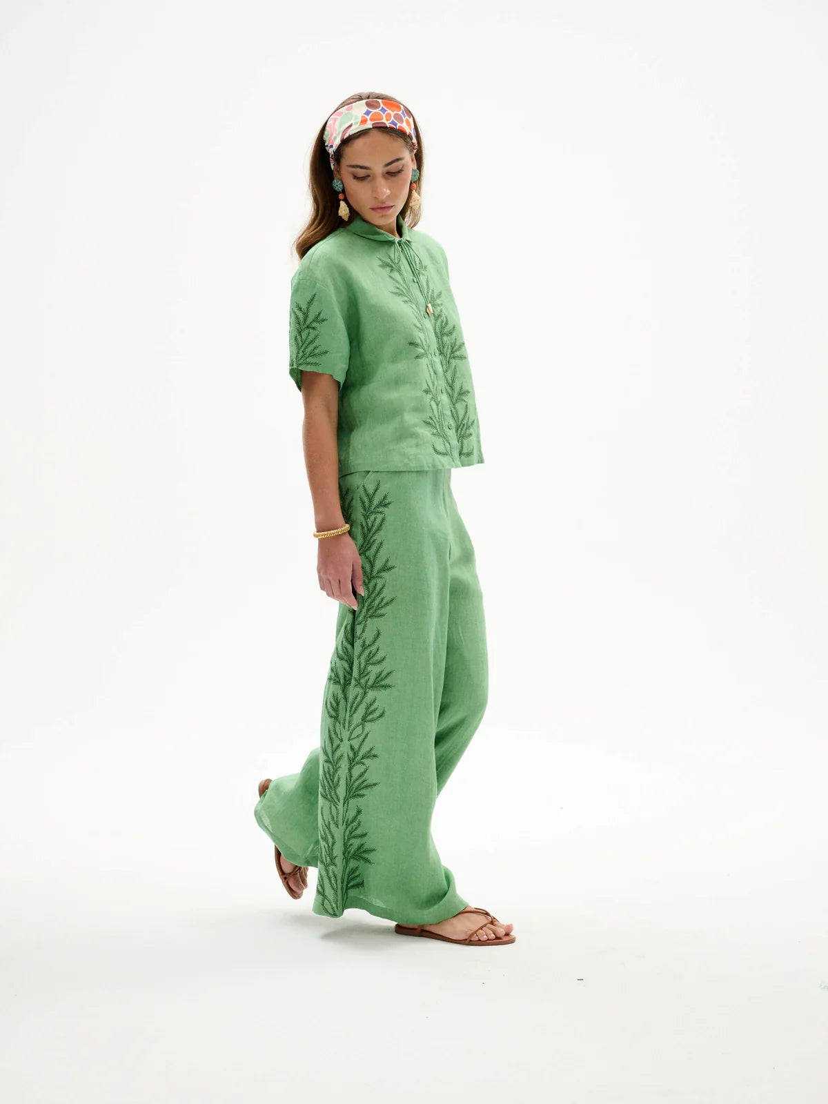 A woman modeling a sage green two-piece linen set with embroidered leaf patterns, featuring a short-sleeve top and matching wide-leg pants, against a plain white studio background.