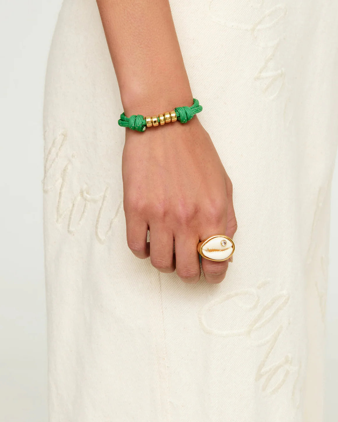 Hand wearing a green and gold bracelet on a white textured background
