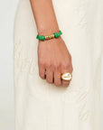 Hand wearing a green and gold bracelet on a white textured background