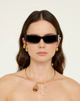 Woman wearing black sunglasses and gold jewelry against a white background