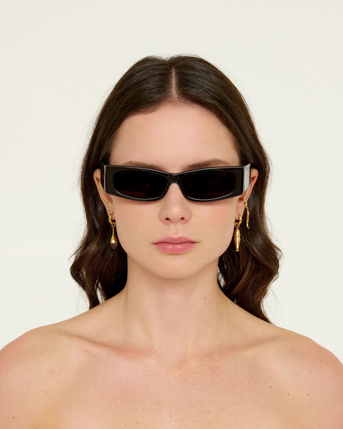 Woman wearing black sunglasses and gold earrings on a white background