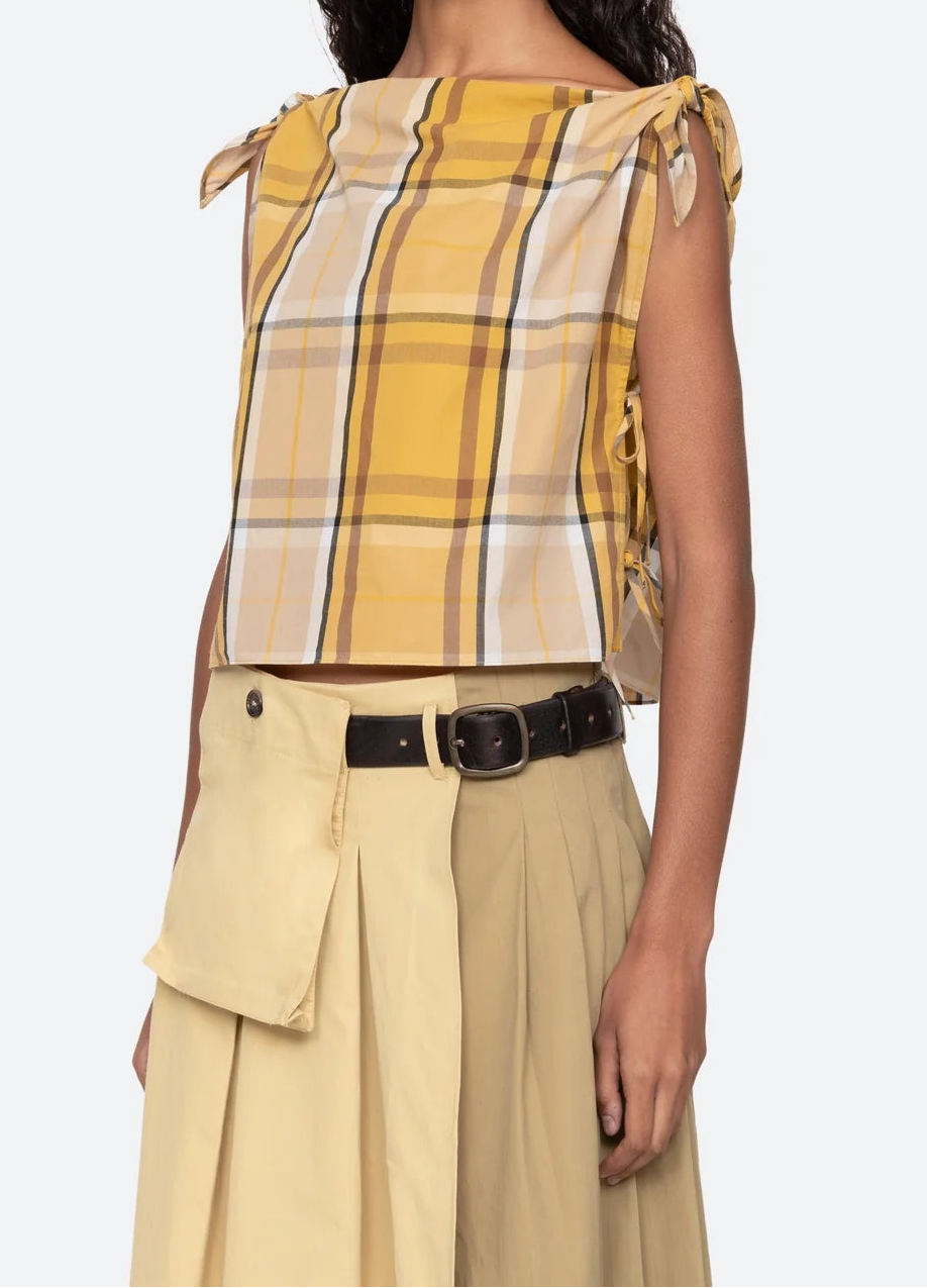 Woman wearing a yellow plaid top and beige pants on a white background
