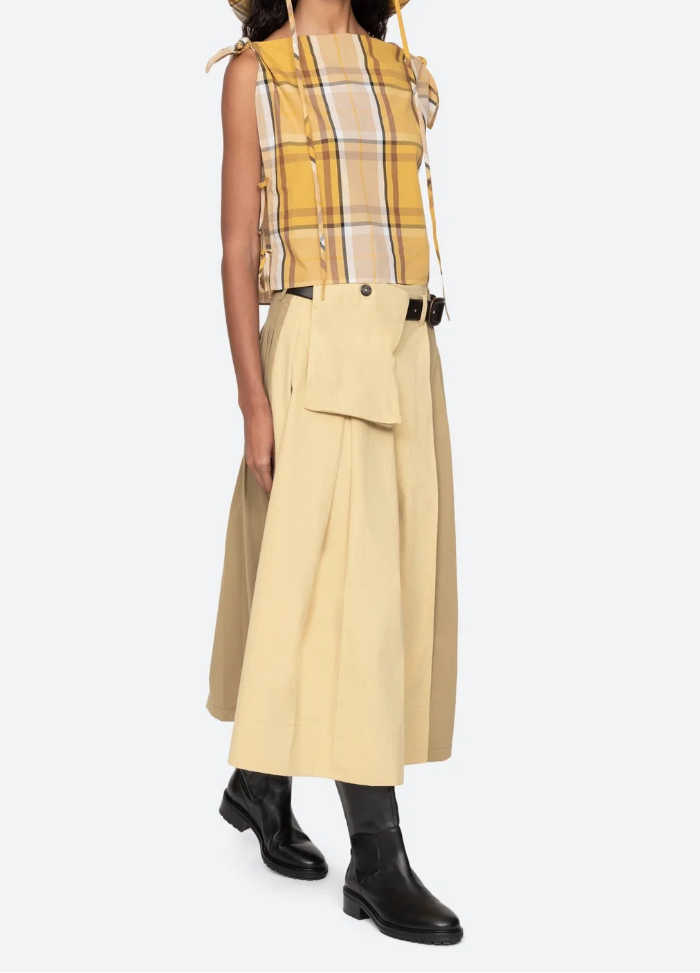 Woman wearing a yellow plaid top and beige skirt with a white background