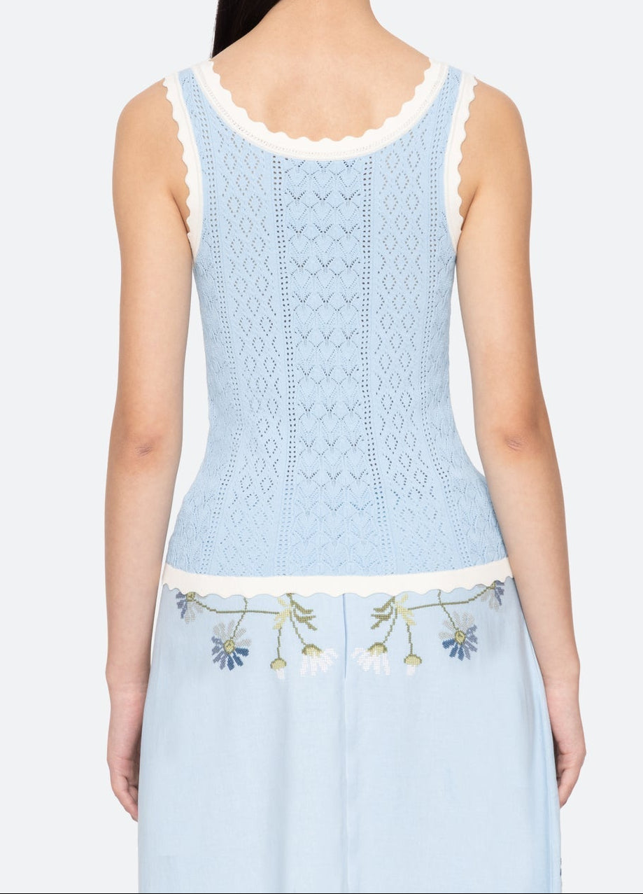 Woman wearing a light blue sleeveless top with floral embroidery on a plain background