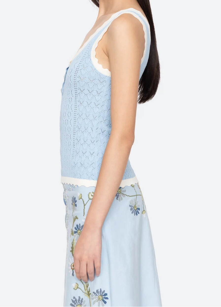 Woman wearing a light blue sleeveless top and skirt with floral patterns on a white background