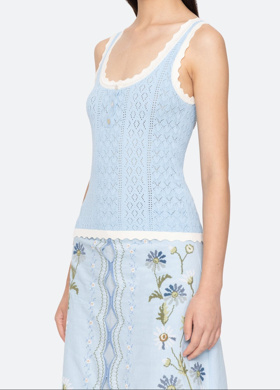 Woman wearing a light blue sleeveless top and floral skirt on a white background