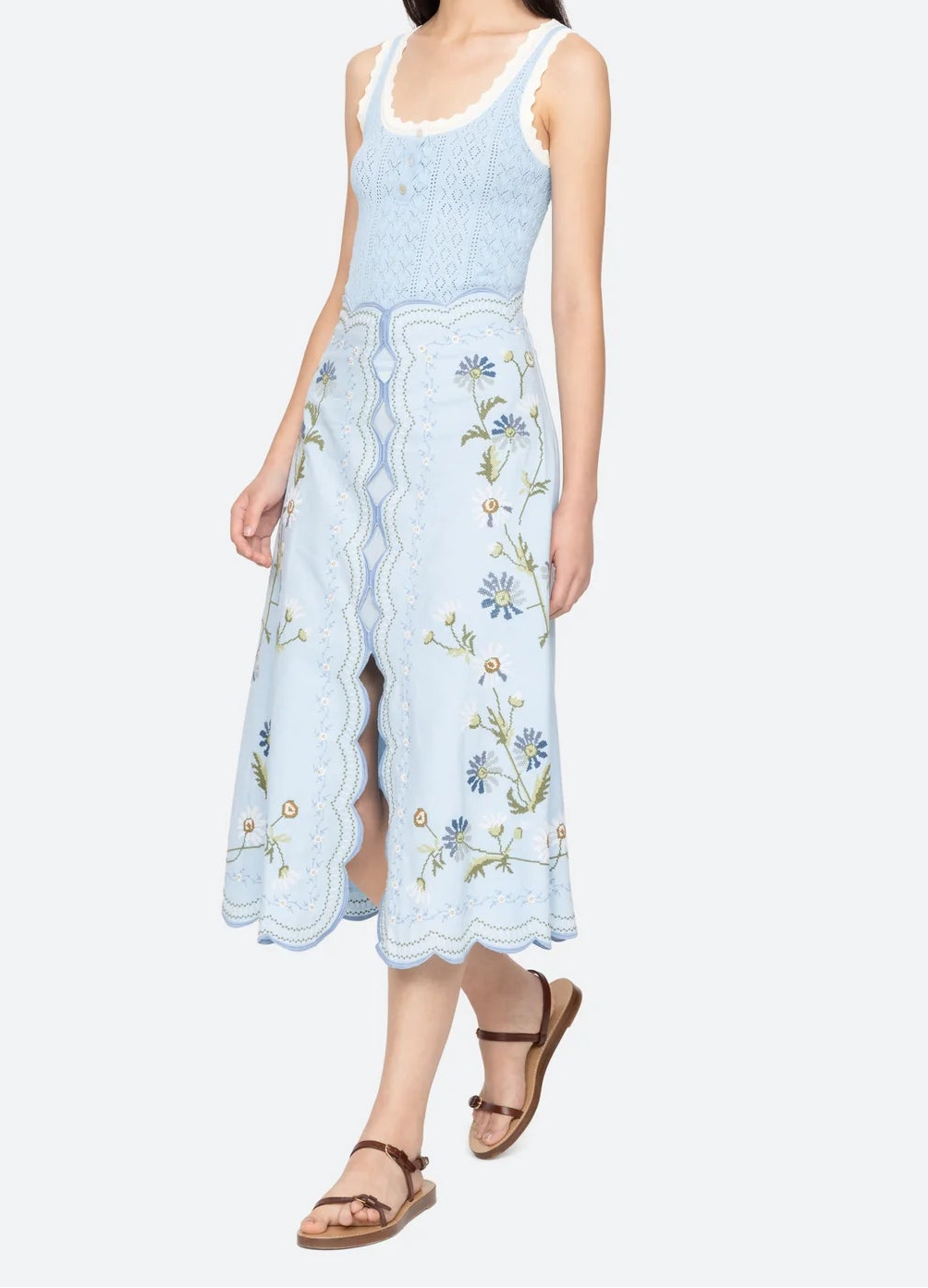 Woman wearing a light blue sleeveless top and floral embroidered skirt on a white background