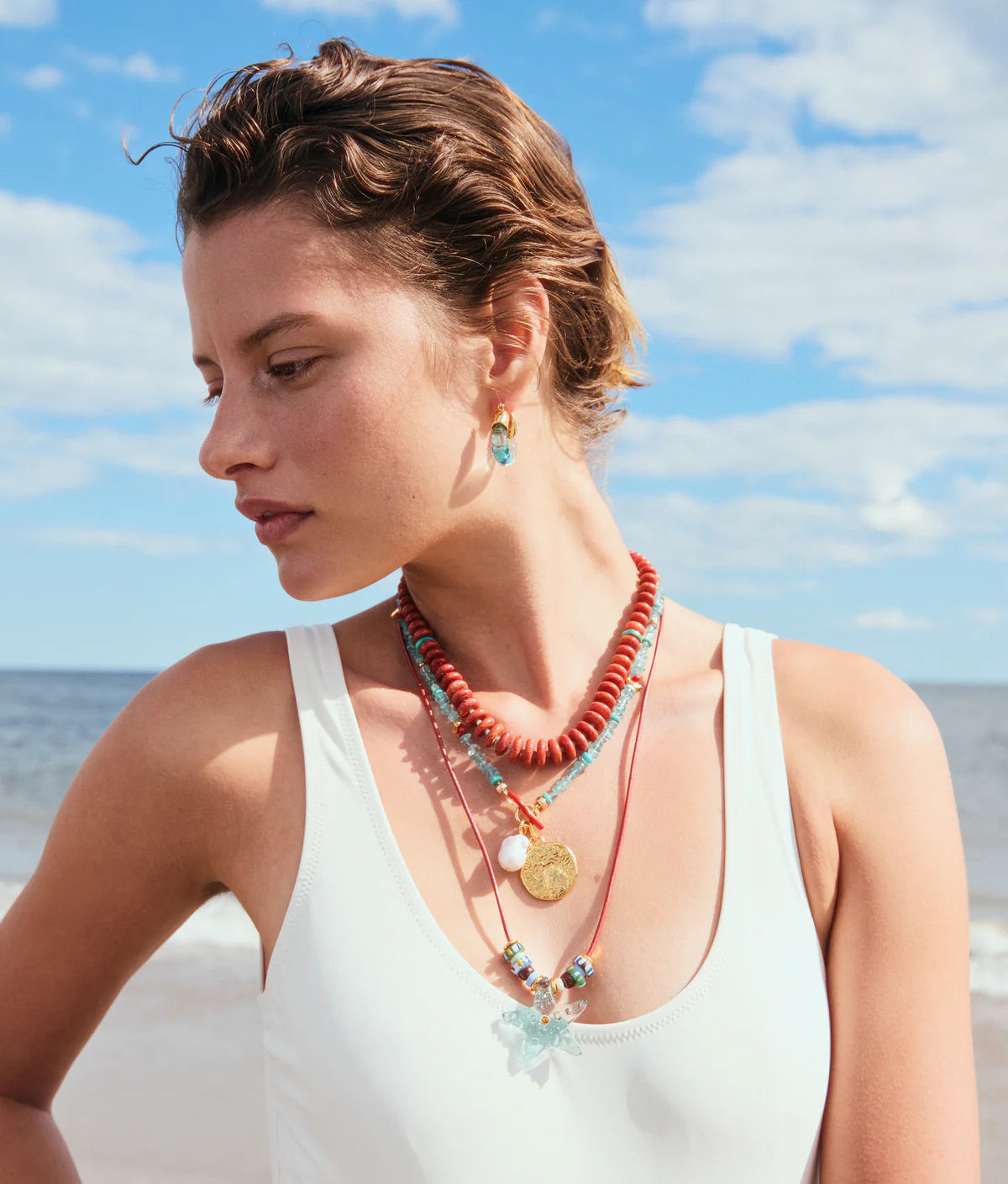 Woman wearing colorful necklaces on a beach with blue sky and ocean in the background